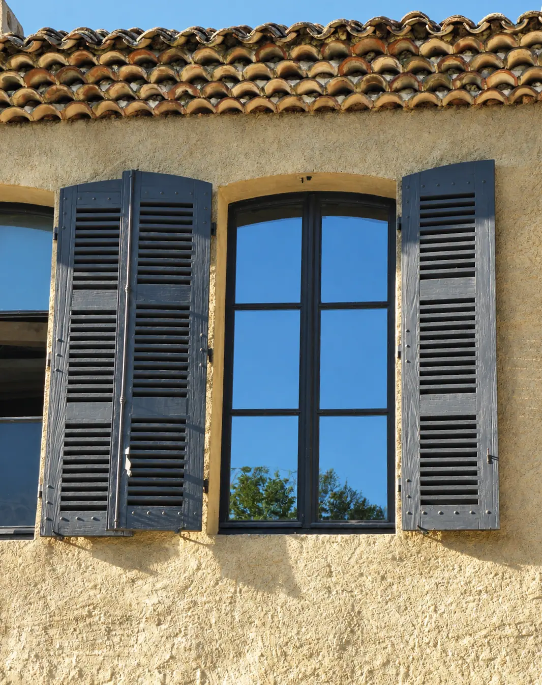 Fenêtre bois sous génoise, persiennes bleues ouvertes sur un mur ocre