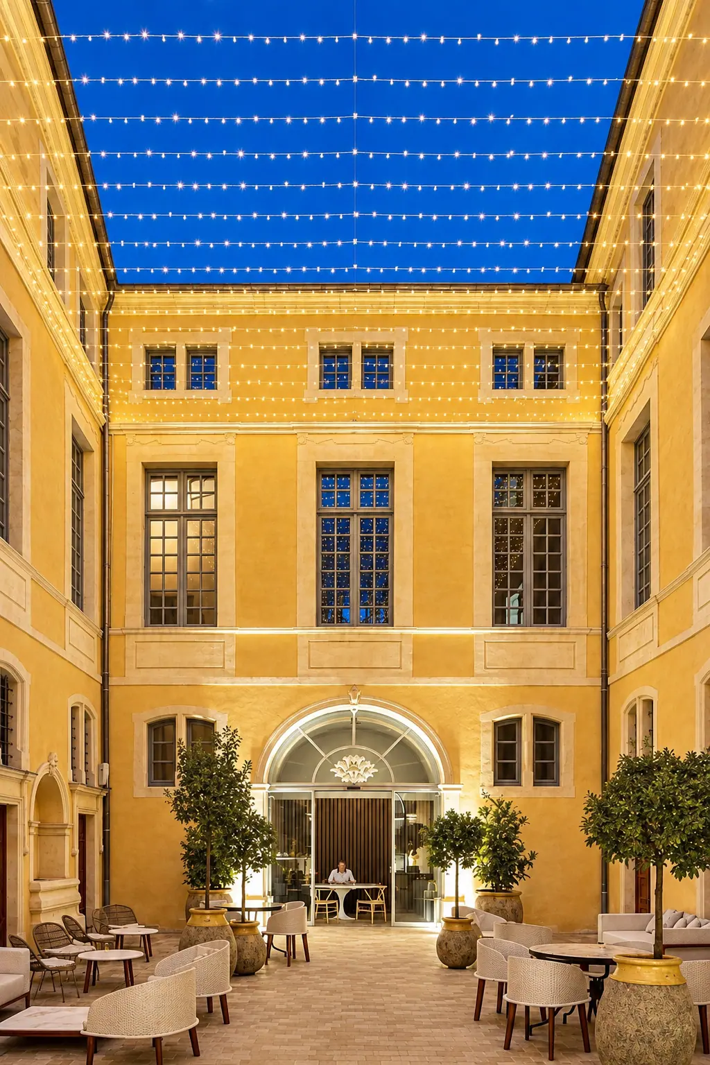 Cour de l'Hôtel Chouleur à Nîmes sous un ciel de guirlandes, façades ocre et menuiseries bois
