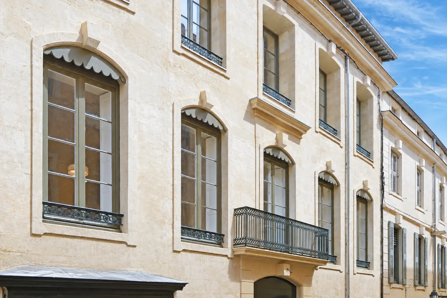 Façade en pierre du 7 rue Fresque à Nîmes, fenêtres bois cintrées et balcons en fer forgé