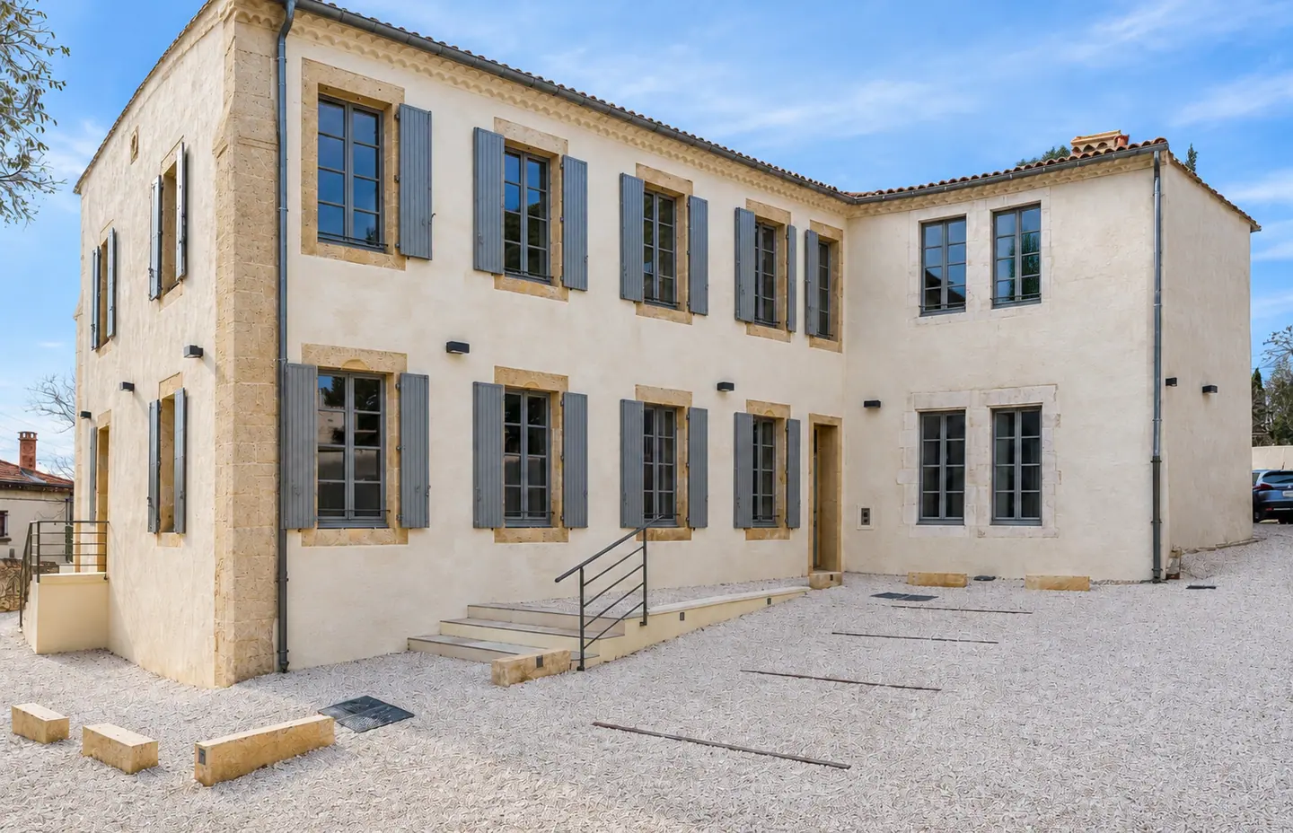 Façade de pierre blonde du 9 rue de la Poudrière à Nîmes, fenêtres bois et volets bleus autour d'une cour