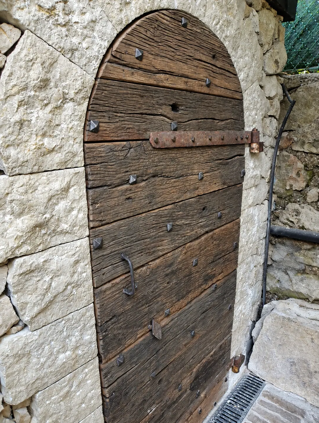 Porte ancienne en planches et pentures forgées dans un mur de pierre