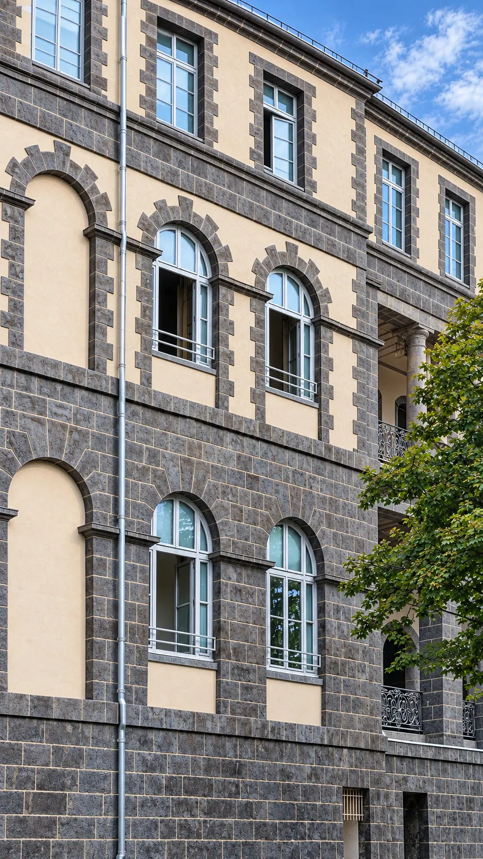 Façade de basalte et de pierre claire percée de fenêtres cintrées
