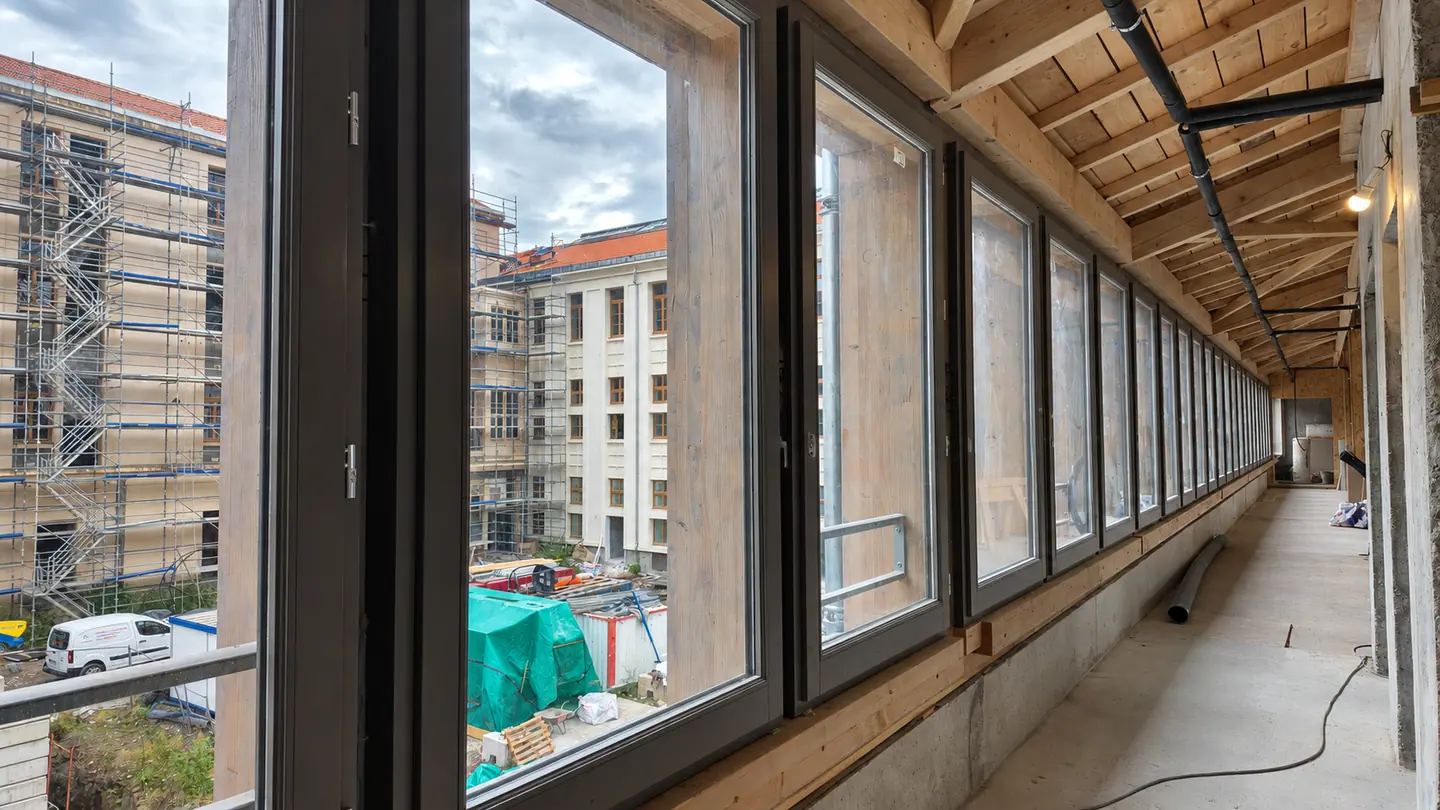Longue galerie éclairée par une file de fenêtres bois, vue sur le chantier