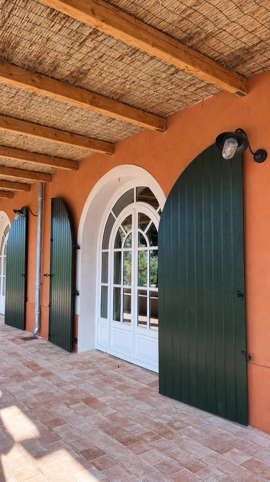 Galerie couverte de canisses, porte-fenêtre cintrée et volets pleins verts