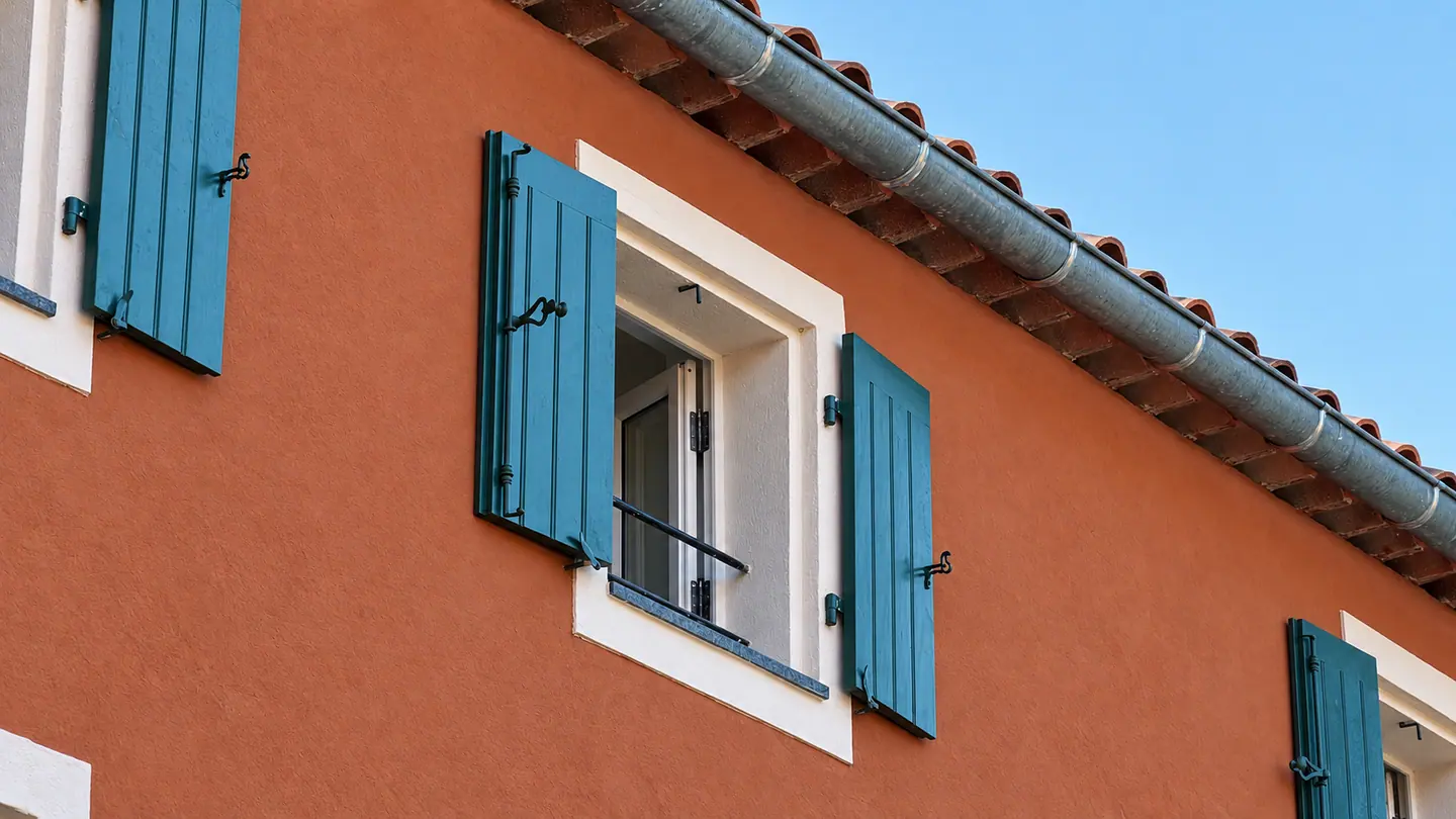 Façade ocre rouge rythmée de volets bois verts