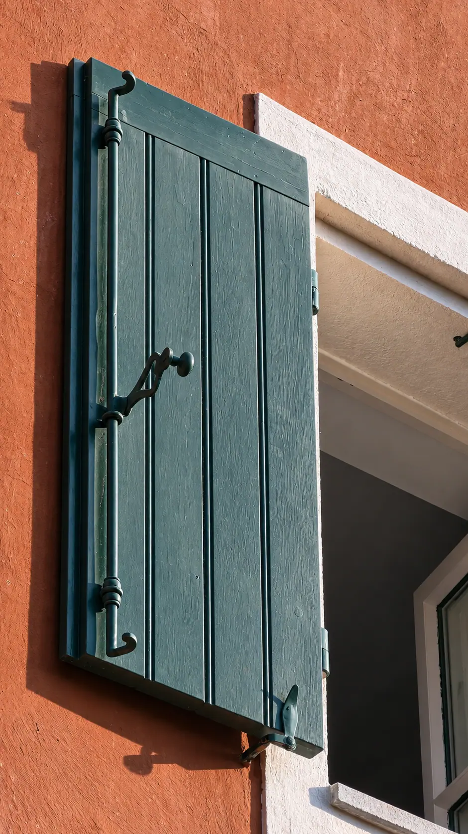 Volet bois vert à lames verticales et pentures, entrouvert sur la façade